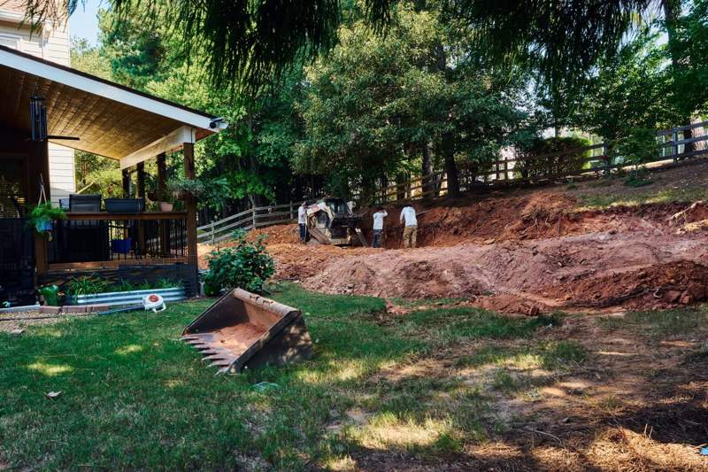 crew excavating the backyard slope with a compact track loader before the retaining wall build in Forsyth County GA