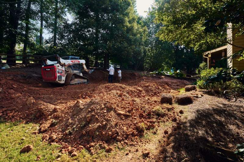 compact track loader and crew moving red clay to prepare the retaining wall footing