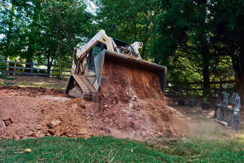 compact track loader dumping a bucket of red clay during excavation for the retaining wall